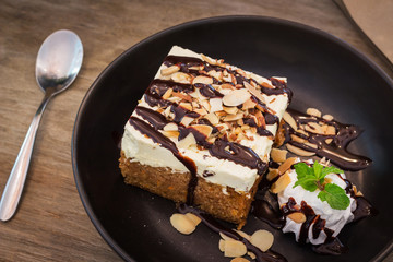 Carrot cake with fresh cream topping slice almond and chocolate sauce on a wooden background