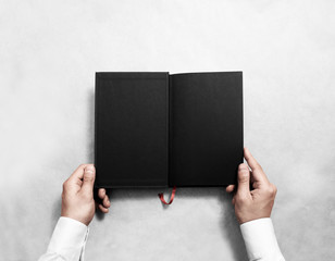 Hand holding blank opened book mock up with black half title. Person reading empty paperback mockup. Black notebook inside template. Publication design leafing man. Textbook spread with bookmark.