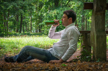 Drunk man lies on the ground near bench with a beer bottle