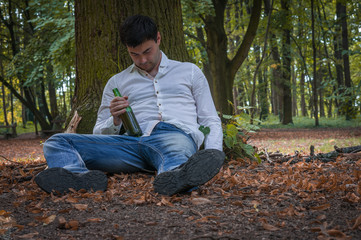 Drunk man lies on the ground under the tree with a beer bottle