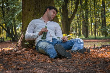 Drunk man lies on the ground under the tree with a beer bottle