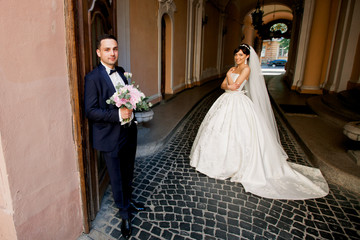 Handsome groom with bouquet and pretty bride in amazing dress