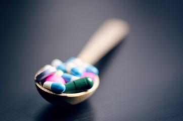 Full wooden spoon of pills. Pharmacy background on a black table. Tablets on a black background. Pills. Medicine and healthy. Close up of capsules. Differend kind of pills 