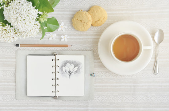 The Time of Tea Break on the table top view. beautiful tablecloth with cup, spoon, notebook, pencil, cookies and white flower with copy space