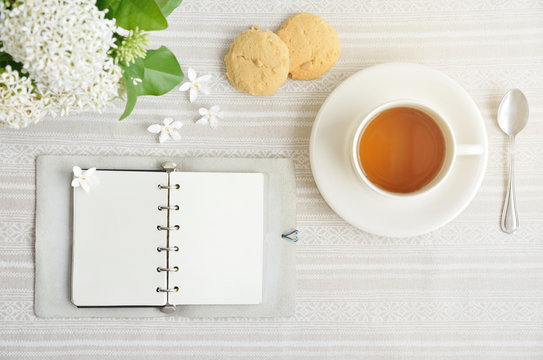 The Time of Tea Break on the table top view. beautiful tablecloth with cup, spoon, notebook,  cookies and white flower with copy space