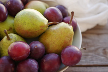Ripe fresh pears and plums in a bowl on a wooden background close up. Autumn harvest of fruit.