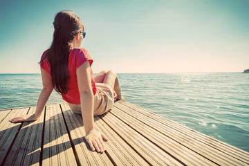 Young woman resting on jetty looking at the calm sea on sunny summer day.