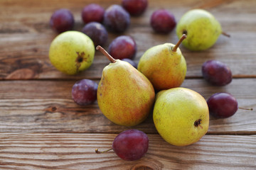 Naklejka na ściany i meble Ripe fresh pears and plums on a wooden background close up. Autumn harvest of fruit.