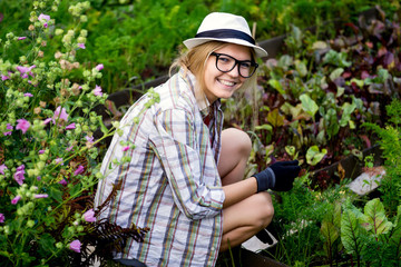Young blonde woman gardener cares for the plants in garden