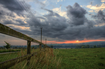 Old wooden fence and electrical power line with dramatic clouds during sunset