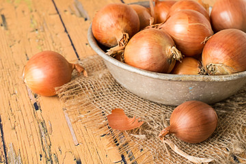 Onion.   Onions in an old aluminum bowl on a wooden table.
