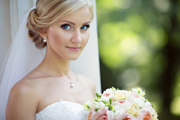 Beauty bride in bridal gown with bouquet and lace veil in the na