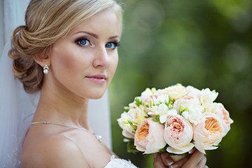 Naklejka premium Beauty bride in bridal gown with bouquet and lace veil in the na
