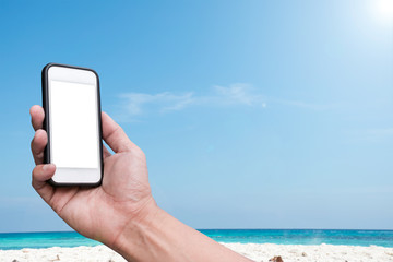 Hand holding Smartphone over beach and blue sky background