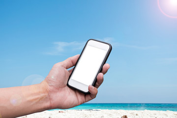 Hand holding Smartphone over beach and blue sky background