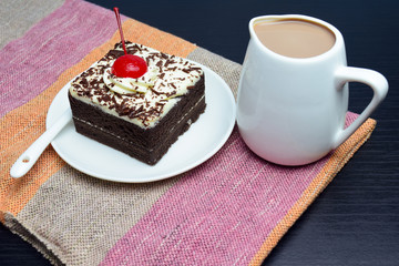 Chocolate cake with cherry and milk jug on plate  mat
