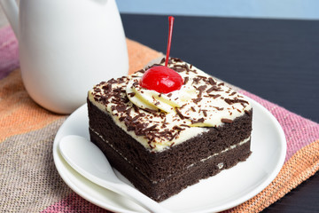 Chocolate cake with cherry and milk jug on plate  mat