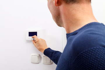 Men regulate temperature on control panel of central heating at wall in living room.