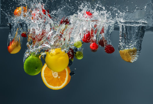 Fototapeta Different fruits and berries falling in water on dark background