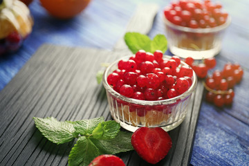 Fresh red currant and orange in glass bowl on cutting board