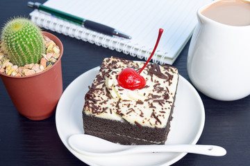 Chocolate cake with cherry and milk jug, cactus, notebook on bla