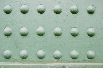 Old metal surface with rivets painted with green paint. A fragment of the armored element of artillery.