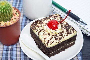 Chocolate cake with cherry and milk jug, notebook on plate mat