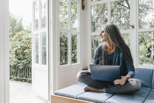 Woman with laptop sitting on lounge in winter garden looking through opened terrace door
