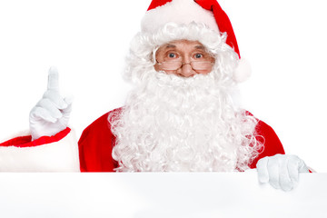 Traditional Santa Claus pointing up and holding white banner on white background. Copy space