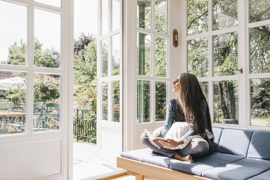 Fototapeta Woman sitting with book on lounge in winter garden looking through opened terrace door