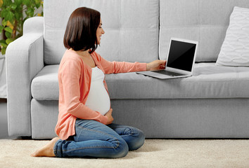 Pregnant woman with laptop sitting on floor