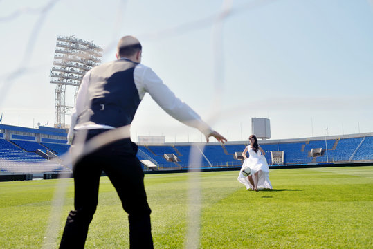 Wedding couple on the football stadium is playing. Beautiful girl in white dress. Man in suit. Beauty bride with groom. Female and male portrait. Woman with lace veil. Lady and guy outdoors