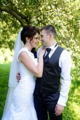 Wedding couple on the nature is hugging each other. Beautiful model girl in white dress. Man in suit. Beauty bride with groom. Female and male portrait. Woman with lace veil. Lady and guy outdoors