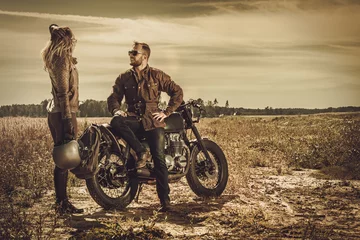 Cercles muraux Moto Stylish cafe racer couple on the vintage custom motorcycles in a field.