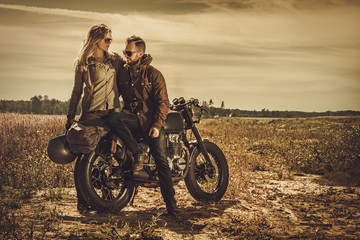Couple de café racer élégant sur les motos personnalisées vintage dans un champ.