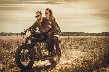 Obraz na płótnie Canvas Stylish cafe racer couple on the vintage custom motorcycles in a field.