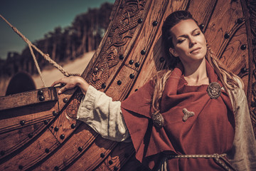 Viking woman standing near Drakkar on the seashore.