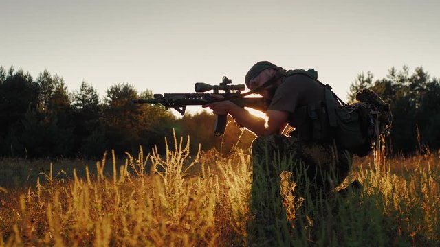 Armed men in camouflage. It takes aim at the optical sight. On the Sunset
