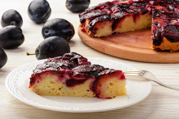 Plum bisquit cake on white wooden background.