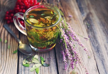Herbal tea in a transparent glass mug, berries of a guelder-rose and forest herbs on a wooden surface of a table. Tea from autumn herbs and berries. Phytotea   