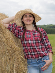 Portrait of young woman standing next to a stack of hay in sunlight