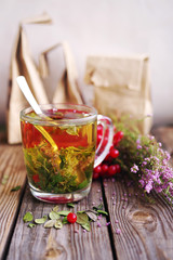 Herbal tea in a transparent glass mug, berries of a guelder-rose and forest herbs on a wooden surface of a table. Tea from autumn herbs and berries. Phytotea   