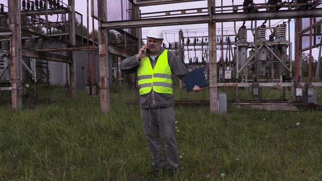 Electrician with folder using smartphone in electrical substation