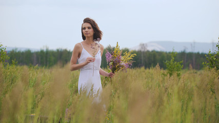 Fototapeta na wymiar Summer flowering field and a beautiful girl in a white sundress.