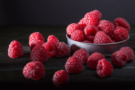 Many raspberries in small steel bowl and near on dark wooden bac