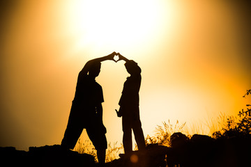 Silhouetted friend forming a heart symbol at golden hour sunset