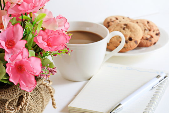 Delicious Homemade Cookies with chocolate chips, white cup of coffee and beautiful flowers on white wooden tacle