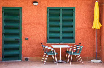 Fototapeta na wymiar Modern house entrance colorful Italian with table and chairs and umbrella