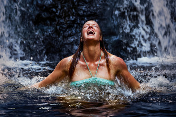 Young beautiful woman at waterfall jumping to wild river