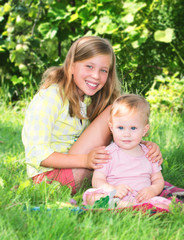 Naklejka na ściany i meble Two adorable sisters outdoors. Smiling girls sitting on the grass